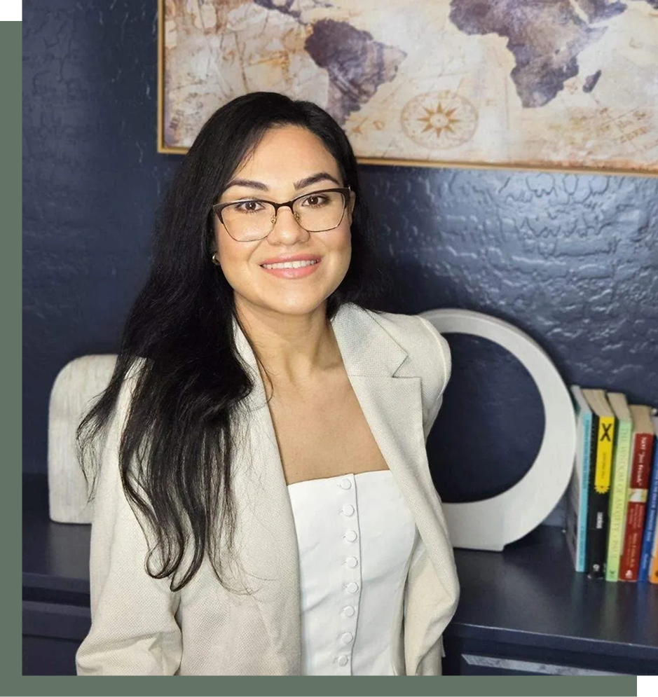 A woman with glasses smiling at the camera in an office setting.