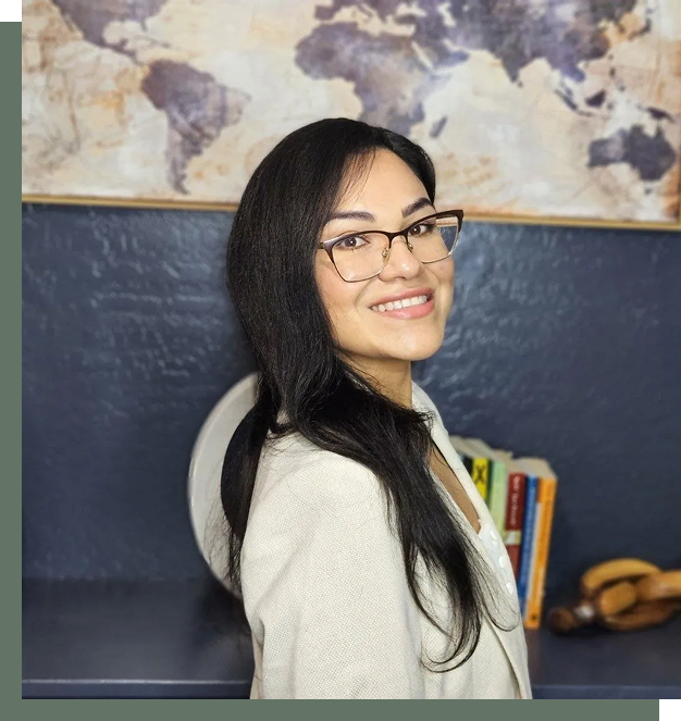 Smiling woman with glasses posing indoors against a blue wall.