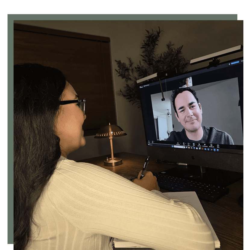 A woman video chats with a man on a computer screen in a cozy room.